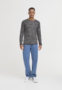 Lange mouwen, ronde hals trui in een zwart en grijs gespikkeld patroon, gecombineerd met lichtblauwe recht gesneden jeans en witte sneakers.