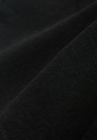 Schwarzer Stoff mit weicher Textur, gezeigt in Falten, die eine glatte, gleichmäßige Webart hervorheben. Es sind keine Muster oder Akzente sichtbar.