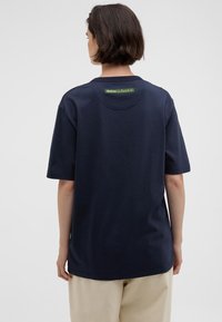 T-shirt de algodão azul-marinho com mangas curtas, corte descontraído e decote redondo. Etiqueta da marca verde na parte superior das costas. Textura suave.