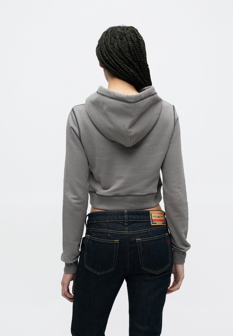 Gray cropped hoodie with a hood, featuring contrasting stitching. Paired with dark blue jeans, showcasing a label at the waistband.