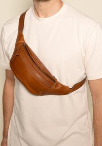 Hnědý kožený ledvinka s zakřiveným designem, obsahující přední zipovou kapsu, prošívání a nastavitelné popruhy.