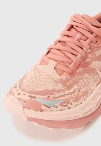 Chaussure de sport rose avec une tige en tissu texturé, présentant des sections en maille, une pointe renforcée et une semelle superposée avec un motif abstrait ondulé.