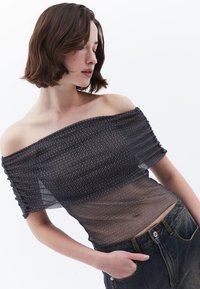 Sort off-the-shoulder top med et gennemsigtigt, struktureret design med horisontale striber. Båret med højtaljede denim jeans.