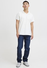 Hvit polo skjorte med krage, kombinert med mørkeblå denim jeans. Grå sneakers fullfører antrekket. Enkelt og uformelt design.
