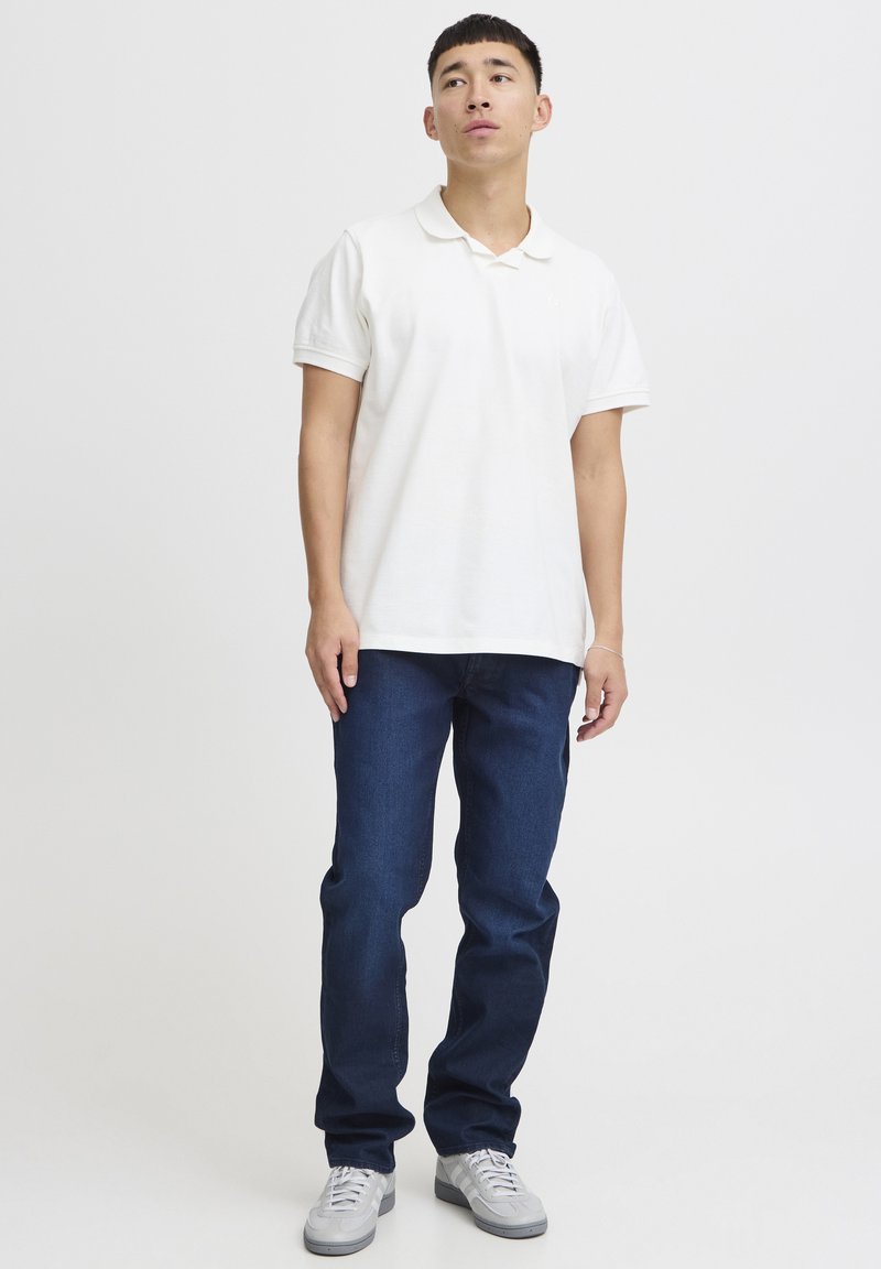 Hvit polo skjorte med krage, kombinert med mørkeblå denim jeans. Grå sneakers fullfører antrekket. Enkelt og uformelt design.