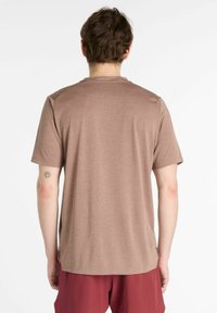 Brown, short-sleeve T-shirt with a textured fabric, rounded neckline, and side slits. Worn with maroon shorts.