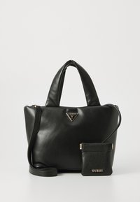 Zwarte leren Guess handtas met gewatteerde handvatten en een afneembare kleine tas met gouden logo's en een schouderriem, op een witte achtergrond.