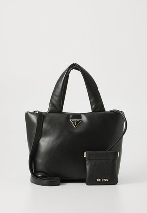 Zwarte leren Guess handtas met gewatteerde handvatten en een afneembare kleine tas met gouden logo's en een schouderriem, op een witte achtergrond.