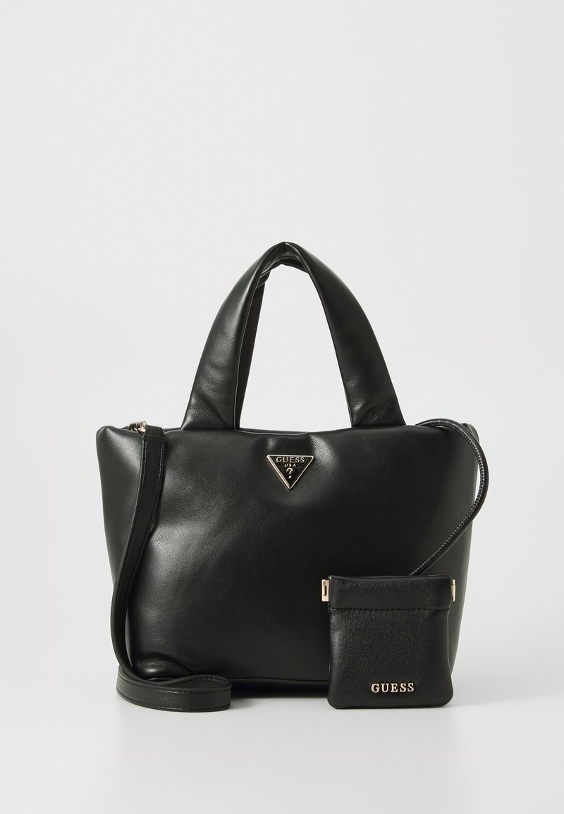 Zwarte leren Guess handtas met gewatteerde handvatten en een afneembare kleine tas met gouden logo's en een schouderriem, op een witte achtergrond.