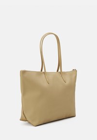 Beige nylon bevásárlótáska, két textúrált fogantyúval, téglalap alakú, és cipzárral zárható a tetején. Simaság jellemzi, minimális részletezéssel.