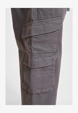 I pantaloni cargo realizzati in tessuto grigio scuro presentano numerose tasche laterali, cuciture rinforzate e una vestibilità comoda. Texture liscia con una leggera lucentezza.