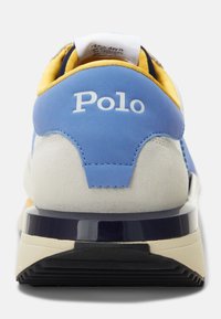 Blå och gul sneaker med mocka och mesh-material. Har en vit logotyp, texturerade accenter och en mörk sula med en glänsande finish.