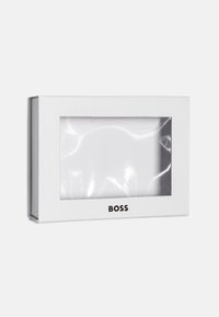 Boîte rectangulaire blanche avec une fenêtre en plastique transparente affichant un article en tissu blanc plié, marqué du texte "BOSS" en dessous de la fenêtre.