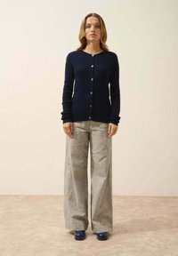 Granatowy sweter dziergany z teksturowanym wzorem, z zapięciem na guziki i długimi rękawami, zestawiony z jasnoszarymi spodniami o szerokich nogawkach i niebieskimi butami.