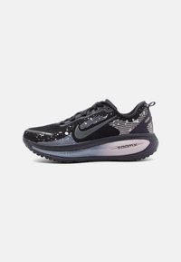 Černé a šedé běžecké boty Nike ZoomX s abstraktními bílými vzory, černým logem swoosh a silnou polstrovanou podrážkou na bílém pozadí.