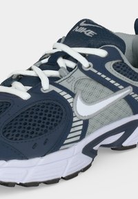 Τρέχον παπούτσι Nike σε μπλε ναυτικό και γκρι χρώμα με λευκά κορδόνια, δίχτυ σε πλαϊνά τμήματα και λευκό λογότυπο Nike Swoosh.
