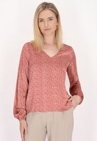 Langærmet bluse i dyb pink stof, med et blomsterprint i guld. V-halsdesign med let løs pasform og elastiske ærmer.