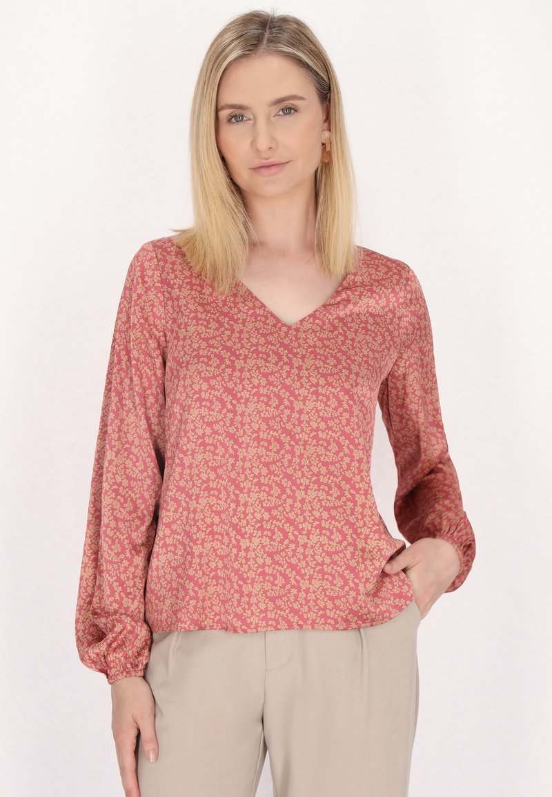 Langærmet bluse i dyb pink stof, med et blomsterprint i guld. V-halsdesign med let løs pasform og elastiske ærmer.