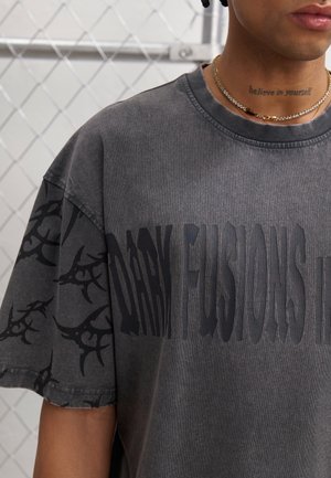 Tmavě šedé oversized tričko s texturovaným černým grafickým designem, krátkými rukávy a žebrovaným kulatým výstřihem.