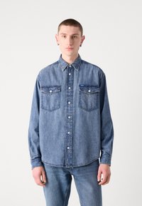 Denim overhemd met knopen in middelblauw, voorzien van een klassieke kraag, twee borstzakken en een licht gebogen zoom. Gemaakt van zachte, textuurrijke stof.