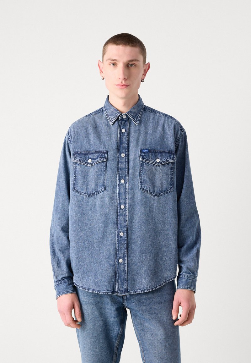 Denimhemd in Mittelblau mit klassischem Kragen, zwei Brusttaschen und leicht abgerundetem Saum. Hergestellt aus weichem, strukturiertem Stoff.