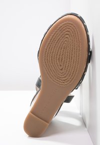 Czarne sandały z ćwiekowanymi akcentami i teksturowaną podeszwą. Płaski obcas i regulowany pasek. Logo widoczne na spodzie buta.