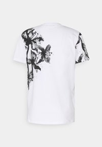 T-shirt branco de mangas curtas com estampado floral preto em um ombro e nas costas, feito de algodão suave, apresentando um decote redondo e um corte relaxado.