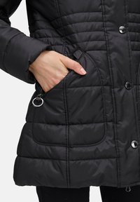 Czarna ocieplana kurtka z pikowanym wzorem w diamenty, z kieszeniami na zamek błyskawiczny i zatrzaskami; gładki, błyszczący materiał o eleganckim fasonie.