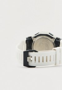 Runde Uhr mit weißem Silikonarmband und schwarzen Akzenten. Verfügt über eine strukturierte Oberfläche und eine metallische Rückseite, sichtbare Schnallendetails.