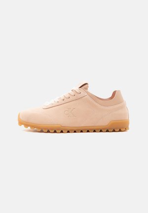 Jasnobeżowy zamszowy sneaker z gumową podeszwą i białymi sznurowadłami, z wytłoczonym logo "cK" po boku.