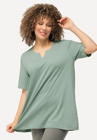 T-shirt verde chiaro a V con maniche corte, in tessuto morbido, vestibilità ampia e orlo curvo, abbinato a pantaloni grigi. Nessun motivo o dettaglio visibile.