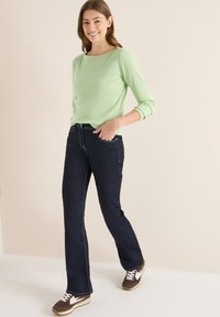 Jasnozielona prążkowana koszula z długim rękawem w zestawie z ciemnoniebieskimi, rozszerzanymi spodniami dżinsowymi z białymi przeszyciami. Do tego brązowe trampki z białymi detalami.