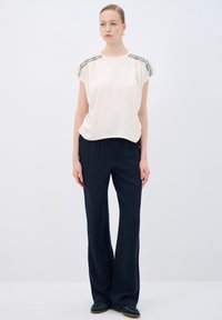 Haut court beige clair à manches courtes avec des détails en perles sur les épaules, associé à un pantalon large navy à coupe décontractée. Tissu lisse, silhouette relaxée.