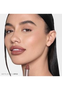 Matte lipstick in de spice tint, gepresenteerd met een zachte, romige textuur. De verpakking is slank en metallic, met moderne designelementen.