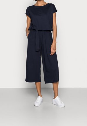 Marine jumpsuit met een top met korte mouwen, een elastische tailleband, brede driekwart pijpen en een bijpassende stoffen riem. Gecombineerd met witte sneakers.