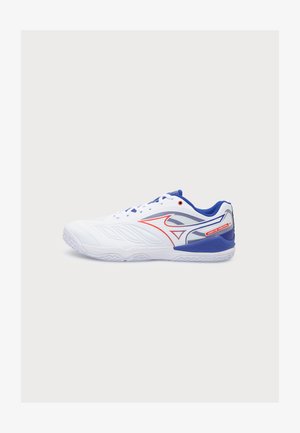 Baskets de sport blanches avec des accents bleus et rouges, design bas, fermeture à lacets et semelle texturée, présentées de profil.