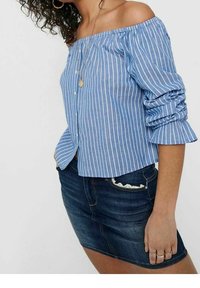 Blusa a righe blu chiaro, scollata sulle spalle, con maniche lunghe e volant; abbinata a una mini gonna in denim scuro e anelli stratificati.