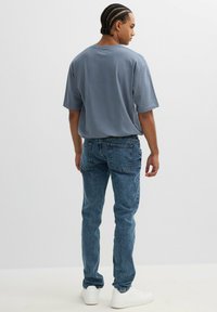Camiseta de algodón gris con un ajuste holgado, combinada con jeans de mezclilla azul de cintura alta y zapatillas blancas. Los jeans cuentan con bolsillos traseros clásicos.