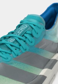 Τυρκουάζ αθλητικό παπούτσι με λεία επάνω επιφάνεια, υφή στα κορδόνια, γκρι λεπτομέρειες και ελαφριά μαλακή σόλα με ετικέτα του бренδου στη γλώσσα του παπουτσιού.