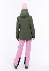 Grüne isolierte Jacke mit Kapuze, kombiniert mit pinken Skihosen, die schwarze Akzente und ein weit ausgestelltes Design aufweisen. Rückansicht.