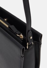 Czarna torebka o sztywnym kształcie, wykonana z teksturowanej skóry. Posiada złote elementy metalowe, zamek błyskawiczny oraz jeden pasek.