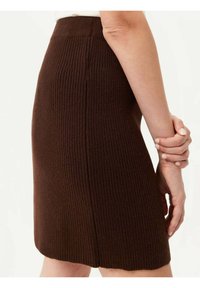Brun ribbad stickad kjol med en åtsittande design. Har en slät midja och en något vågig fåll för extra detaljer och textur.