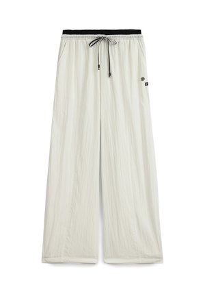 Pantalon beige clair à jambes larges, avec une taille élastique noire et un cordon de serrage noir, orné de petites étiquettes de logo sur le côté droit.