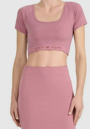 Kobieta ubrana w mauve krótki top z krótkim rękawem z napisem "ATHLTC 4F ALLURE" oraz dopasowaną spódnicę z wysokim stanem na jednolitym tle.
