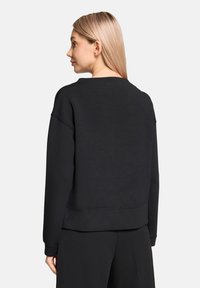 Sweat-shirt noir avec un col rond, une coupe ample et des poignets côtelés. Il présente une texture lisse et une longueur raccourcie.