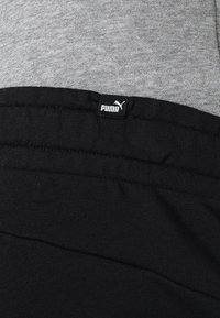 Svarta bomullssweatpants med en grå midja. Logotags placerad på midjan, med en liten vit logotyp på en svart bakgrund.