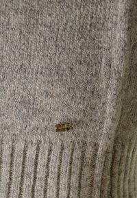 Maglione grigio a maglia con tessuto texturizzato, orlo a coste e un piccolo logo metallico sul davanti.