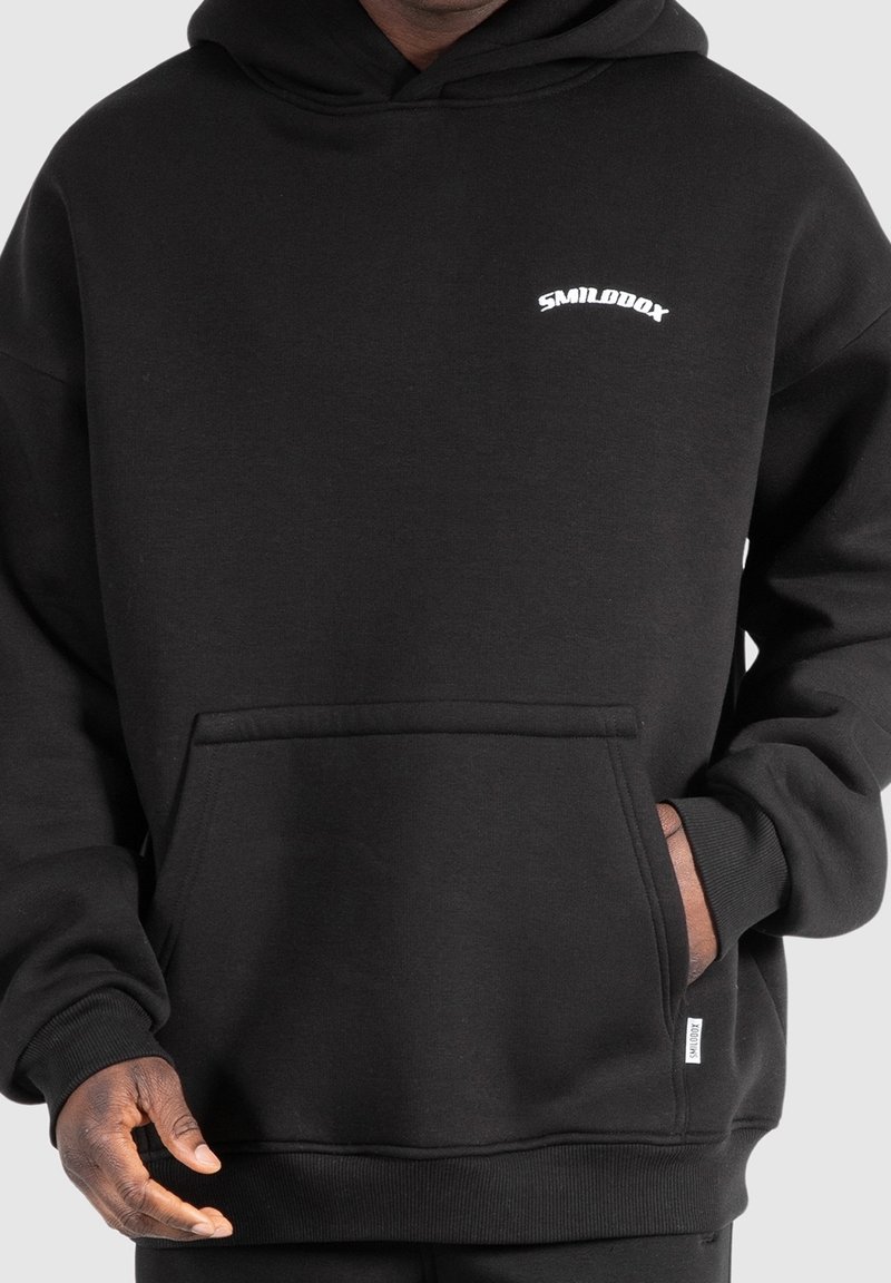 Sweat à capuche en coton noir avec une grande poche avant, des poignets côtelés et un petit logo blanc sur la poitrine. Texture douce et coupe décontractée.