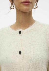 Ivory gebreide cardigan met een ronde halslijn, voorzien van een textuurstof, zachte afwerking en zwarte knoopsluitingen aan de voorkant.