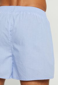 Boxers en tissu à carreaux bleu clair avec une taille élastique et une texture lisse, présentant un design simple sans matériel ou accents visibles.